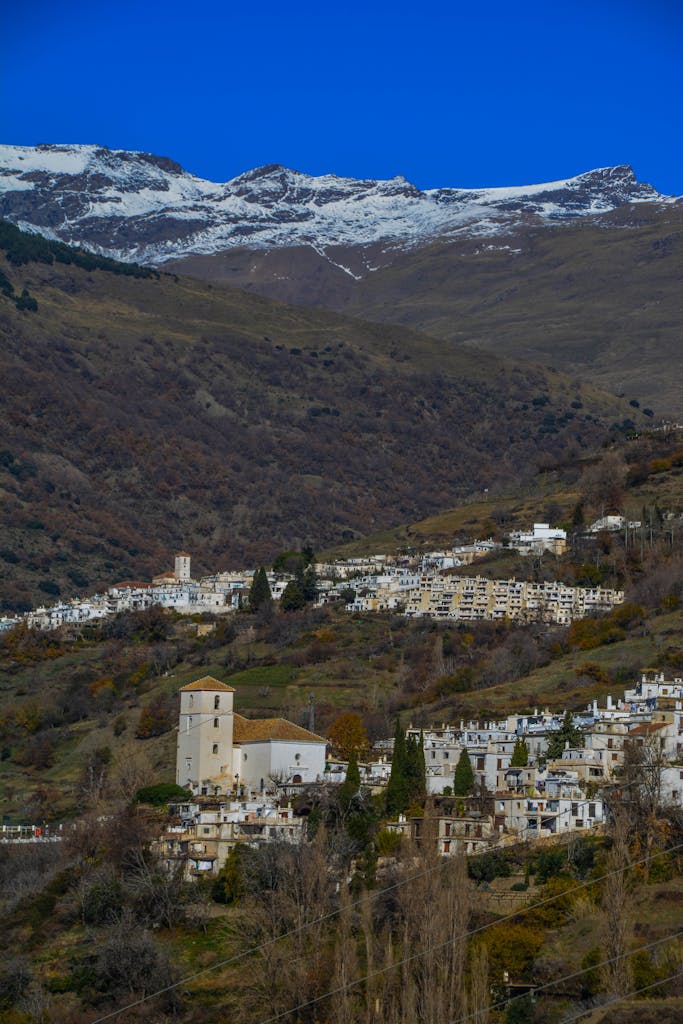 Picturesque Capileira in Spain's Alpujarras with vibrant fall colors and snowcapped mountains.